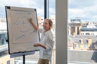 Eve writing on a flip chart at office window