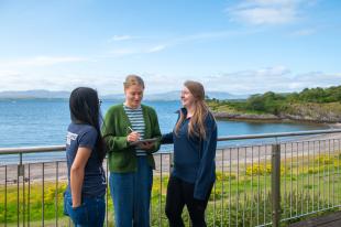 A group of three students chatting with the sea behind