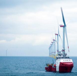 Red boat at sea with offshore wind turbines in the background