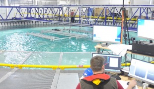 Flowave Ocear Research Facility, student sat at desk with computer in front of wave tank and scaffold bridge with researcher