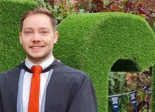 Andrew Russell on graduation day, headshot with green hedge in background